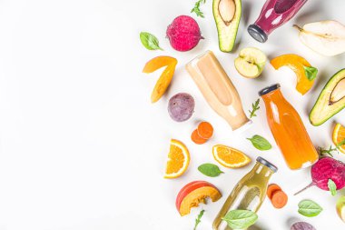Meyve ve sebze püresi konsepti. Porsiyonlu meyve ve sebze suyu şişeleri beyaz masa arkasında taze malzemelerle bezenmiş.