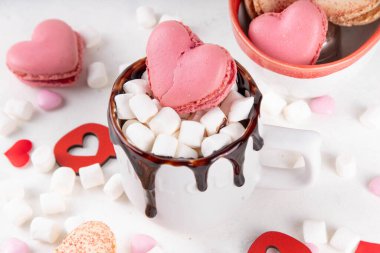 Sevgililer günü sıcak çikolata ya da çikolatalı latte fincanı, kalp şeklinde marşmelov ve makarna kurabiyesi. Tatlı ikramlar içki tarifi fikri, tatlı tatlı içecekler sevgililer günün için.