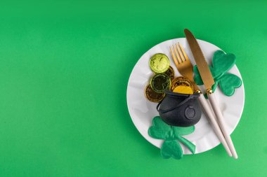 Aziz Patrick Günü şenlik masası. Tabak ve çatal bıçak takımı, altın paralar, leprikon kap, şans için yonca dekoru. Patrick Day menüsü, yeşil arkaplan, parti daveti, üst görünüm kopyalama alanı