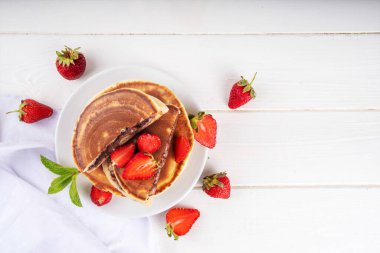 Fındıklı çikolatalı krep yığını. İçinde çikolata sosu olan tatlı kahvaltı krepleri ve beyaz mutfak masasında taze mercanlar.