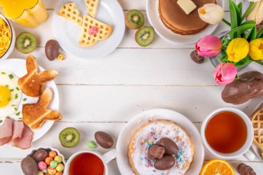 Paskalya tatili tatlı kahvaltı, brunch. Paskalya süslü Belçika waffle 'ları, krepler, kahvaltı gevrekleri ve süt, kızarmış yumurtalar kızarmış ekmek ve pastırma, Paskalya çikolatalı yumurtalar ve bahar çiçekleriyle birlikte tavşan.
