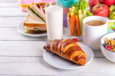 Okul çocukları için sağlıklı besleyici bir sabah kahvaltısı, taze meyve, sebze, kruvasan, müsli, süt ve sandviç. Okuldan ve işten önce kahvaltı yapmak, fotokopi çekmek.