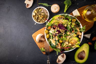 Bitki temelli keto yiyecekler, düşük karbonhidratlı vegan salatası çeşitli yeşil sebzeler, avokado, roka, ıspanak, marul, beyaz peynir, fındık, fıstık, fıstık ezmesi, avokado ve zeytin.