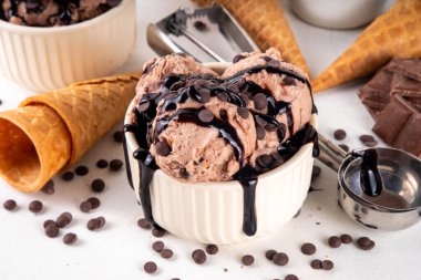 Beyaz masa arkasında dondurma külahlı duble çikolatalı dondurma kasesi. Ev yapımı çikolatalı dondurma ve çikolata sosu, tatlı ve lezzetli yaz tatlısı.