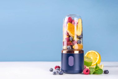 Portatif blender, meyve suyu, meyve suyu ve milkshake 'te sağlıklı meyve suyu ve meyve suyu. Şeffaf blender bardakta meyveler ve masa arkasında taze meyve suyu bardakları.