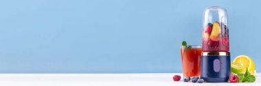 Portatif blender, meyve suyu, meyve suyu ve milkshake 'te sağlıklı meyve suyu ve meyve suyu. Şeffaf blender bardakta meyveler ve masa arkasında taze meyve suyu bardakları.