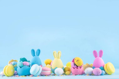 Tatlı ve parlak pastel renkli Paskalya yumurtaları ve tavşan arka planı. Pembe. Mavi, sarı renkli tavşanlar, yuvalarda ve yumurta kabuklarında çikolata yumurtaları, açık mavi arkaplanda şeker parçacıkları