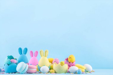 Tatlı ve parlak pastel renkli Paskalya yumurtaları ve tavşan arka planı. Pembe. Mavi, sarı renkli tavşanlar, yuvalarda ve yumurta kabuklarında çikolata yumurtaları, açık mavi arkaplanda şeker parçacıkları
