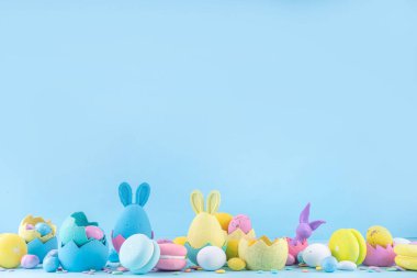 Tatlı ve parlak pastel renkli Paskalya yumurtaları ve tavşan arka planı. Pembe. Mavi, sarı renkli tavşanlar, yuvalarda ve yumurta kabuklarında çikolata yumurtaları, açık mavi arkaplanda şeker parçacıkları