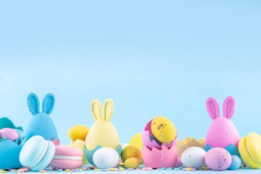 Tatlı ve parlak pastel renkli Paskalya yumurtaları ve tavşan arka planı. Pembe. Mavi, sarı renkli tavşanlar, yuvalarda ve yumurta kabuklarında çikolata yumurtaları, açık mavi arkaplanda şeker parçacıkları