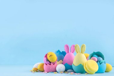 Tatlı ve parlak pastel renkli Paskalya yumurtaları ve tavşan arka planı. Pembe. Mavi, sarı renkli tavşanlar, yuvalarda ve yumurta kabuklarında çikolata yumurtaları, açık mavi arkaplanda şeker parçacıkları