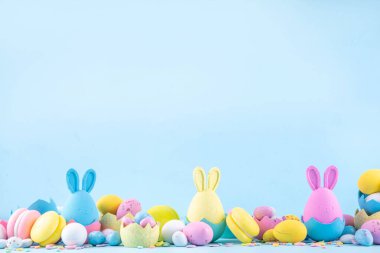 Tatlı ve parlak pastel renkli Paskalya yumurtaları ve tavşan arka planı. Pembe. Mavi, sarı renkli tavşanlar, yuvalarda ve yumurta kabuklarında çikolata yumurtaları, açık mavi arkaplanda şeker parçacıkları