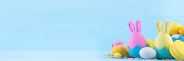 Tatlı ve parlak pastel renkli Paskalya yumurtaları ve tavşan arka planı. Pembe. Mavi, sarı renkli tavşanlar, yuvalarda ve yumurta kabuklarında çikolata yumurtaları, açık mavi arkaplanda şeker parçacıkları