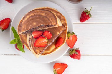 Fındıklı çikolatalı krep yığını. İçinde çikolata sosu olan tatlı kahvaltı krepleri ve beyaz mutfak masasında taze mercanlar.