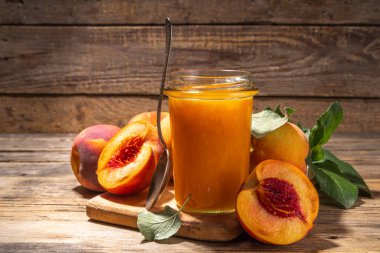 Şeftali reçeli ve ahşap masa arkasında taze şeftali meyveleri.