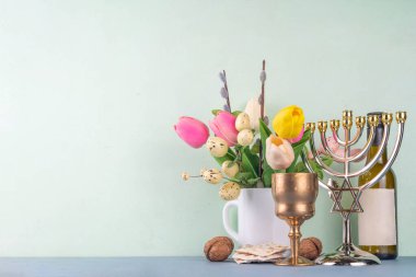 Pesah and Passover Jewish Spring holiday background with spring tulip flowers, decorative Easter eggs, wine bottle and glass, matzah flatbread, nuts and menorah on colorful background clipart