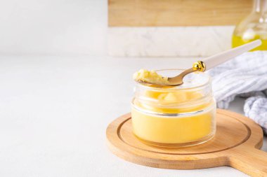 Beyaz mutfak arka planında küçük cam kavanozda ev yapımı kahve yağı, kopyalama alanı. Erimiş organik ghee netleştirilmiş tereyağı, Bio Ayurveda Laktozsuz yüksek kaliteli hayvan yağı kaynağı