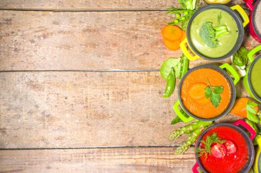 Çeşitli renkte sebze çorbaları. Küçük porsiyonlu kuşkonmaz, ıspanak, brokoli, yeşil bezelye, domates, havuç gibi çeşitli sebze kremalı çorbalar. Ahşap arkaplan kopyalama alanı üst görünümü