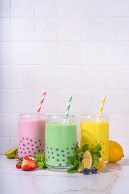 Üç renkli yaz köpüklü çay seti, parlak kremalı inci çayı ya da sütlü tapyoka içecekleri, pembe dut, sarı narenciye, yeşil nane, tapyoka topları ve ezilmiş buz, beyaz arka planda.