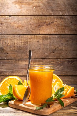 Homemade orange jam in small jar. Homemade orange spicy jam with fresh oranges, cinnamon, mint. Fall preparations and canning on wooden table background copy space
