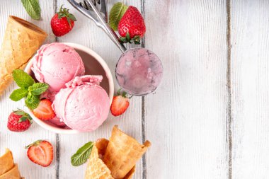 Yaz ferahlatıcı soğuk tatlı, lezzetli ve aromatik çilekli dondurma, seramik kasede ev yapımı meyve şerbeti, taze çilekler, beyaz ahşap arka planda dondurma külahları.