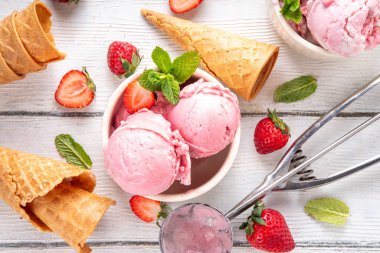 Yaz ferahlatıcı soğuk tatlı, lezzetli ve aromatik çilekli dondurma, seramik kasede ev yapımı meyve şerbeti, taze çilekler, beyaz ahşap arka planda dondurma külahları.