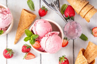 Yaz ferahlatıcı soğuk tatlı, lezzetli ve aromatik çilekli dondurma, seramik kasede ev yapımı meyve şerbeti, taze çilekler, beyaz ahşap arka planda dondurma külahları.