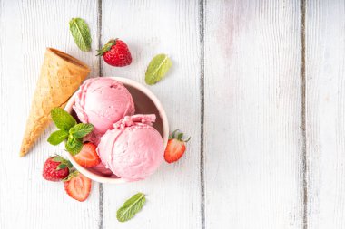 Yaz ferahlatıcı soğuk tatlı, lezzetli ve aromatik çilekli dondurma, seramik kasede ev yapımı meyve şerbeti, taze çilekler, beyaz ahşap arka planda dondurma külahları.