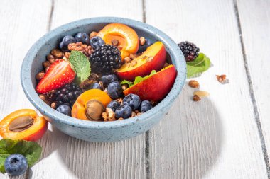 Meyve ve böğürtlenli granola kahvaltısı, yaz tatili lezzetli kahvaltı kasesi bol meyve ve böğürtlenli, süt testisi beyaz ahşap masada.