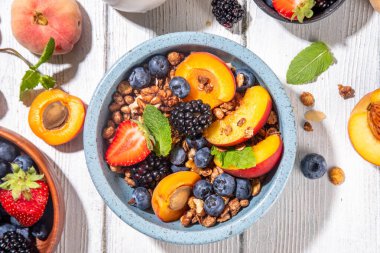 Meyve ve böğürtlenli granola kahvaltısı, yaz tatili lezzetli kahvaltı kasesi bol meyve ve böğürtlenli, süt testisi beyaz ahşap masada.