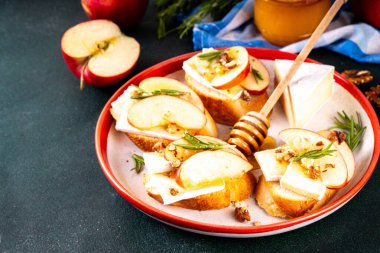 Sonbahar Elmalı Brie Crostini, Ceviz ve Bal, Sonbahar yemeği, Şükran Günü parti aperatifleri. Kırmızı elma dilimli küçük sandviçler, brie peyniri ve tatlı bal çiselemeleri.