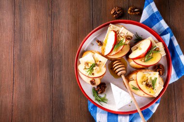 Sonbahar Elmalı Brie Crostini, Ceviz ve Bal, Sonbahar yemeği, Şükran Günü parti aperatifleri. Kırmızı elma dilimli küçük sandviçler, brie peyniri ve tatlı bal çiselemeleri.