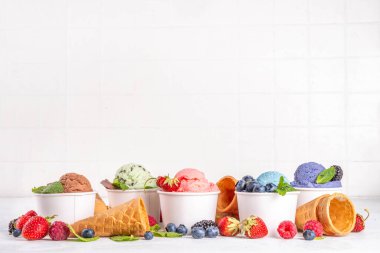 Beyaz arka planda waffle külahları ve böğürtlenlerle dolu renkli dondurmalar. Taze böğürtlenli farklı aromalı dondurma porsiyonları üst görünüm kopya alanı arka planı