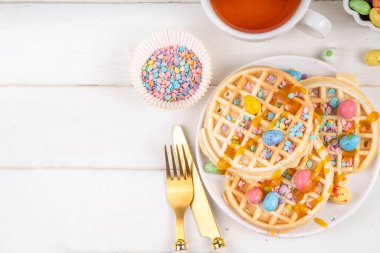 Easter breakfast or brunch. Cute creative decor portion of soft sweet belgian waffles with Easter chocolate eggs, sugar sprinkles and jam or syrup drizzles clipart