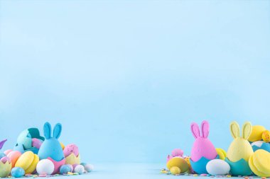 Tatlı ve parlak pastel renkli Paskalya yumurtaları ve tavşan arka planı. Pembe. Mavi, sarı renkli tavşanlar, yuvalarda ve yumurta kabuklarında çikolata yumurtaları, açık mavi arkaplanda şeker parçacıkları