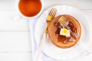 Stack of fresh baked homemade breakfast pancakes with butter and honey or maple syrup drizzles on white wooden table clipart