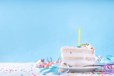 Doğum günü pastası dilimi, parti dekore masasında. Doğum günü pastası beyaz kremalı, şeker serpintili funfetti ve mum, kopyalama alanı