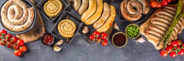 Assortment of different fried sausages. Set with various meat Bavarian, Frankfurt, German grilled sausages, Oktoberfest or summer BBQ party concept, bkack concrete background copy space top view