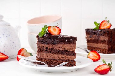 Koyu çikolatalı pasta dilimleri, çikolatalı krema ve çilekli, porsiyonlu tabaklarda, kopyalama alanı