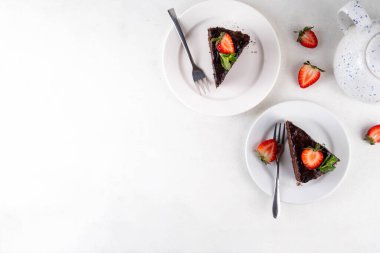 Koyu çikolatalı pasta dilimleri, çikolatalı krema ve çilekli, porsiyonlu tabaklarda, kopyalama alanı
