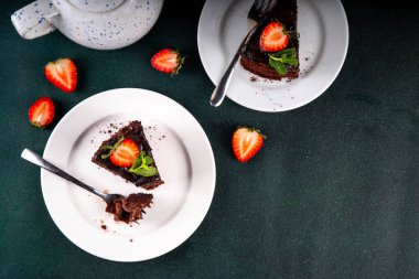 Koyu çikolatalı pasta dilimleri, çikolatalı krema ve çilekli, porsiyonlu tabaklarda, kopyalama alanı