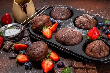 Çilekli çikolatalı kek. Kakao soslu ev yapımı çikolatalı kek tepsisi, şeker tozu ve taze çilek, yabanmersini, koyu kahverengi arka plan fotokopi alanı.