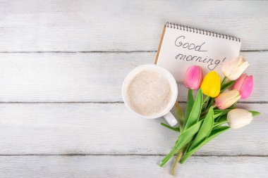 Kahve fincanı ve günaydın notu ve bir buket lale çiçeğiyle dolu bir bahar sabahı. Bahar tatili, tatil arkaplanı, tebrik kartı, üst görünüm düz kopya alanı