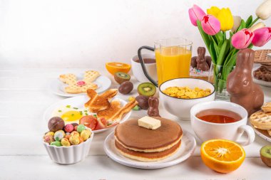 Paskalya tatili tatlı kahvaltı, brunch. Paskalya süslü Belçika waffle 'ları, krepler, kahvaltı gevrekleri ve süt, kızarmış yumurtalar kızarmış ekmek ve pastırma, Paskalya çikolatalı yumurtalar ve bahar çiçekleriyle birlikte tavşan.