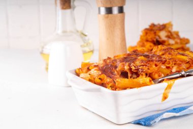 Fırınlanmış Ziti makarnası bolonez ya da marinara domates sosu ve peyniri, fırında tava ve tabakta, beyaz mutfak masasında fotokopi alanı.