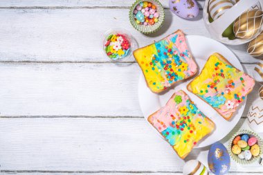 Çocuklar için tatlı ve komik Paskalya kahvaltısı. Ev yapımı gökkuşağı renkli sandviçler, renkli krem peynirli sandviçler ve şeker parçacıkları.