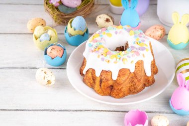 Geleneksel Paskalya pastası şekerleme ve şekerle süslenmiş, şenlikli ruh dekorasyonu ve çiçek buketiyle süslenmiş. Paskalya kutlamaları pastel renkli Paskalya yumurtaları ve tavşan tavşanlarıyla dolu tatil masası.