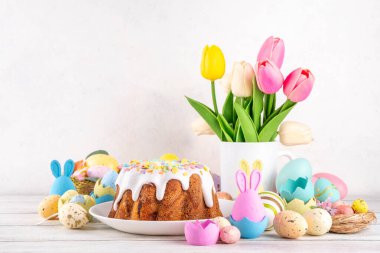 Geleneksel Paskalya pastası şekerleme ve şekerle süslenmiş, şenlikli ruh dekorasyonu ve çiçek buketiyle süslenmiş. Paskalya kutlamaları pastel renkli Paskalya yumurtaları ve tavşan tavşanlarıyla dolu tatil masası.