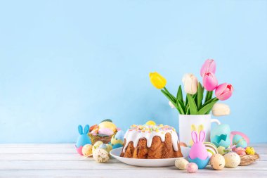 Geleneksel Paskalya pastası şekerleme ve şekerle süslenmiş, şenlikli ruh dekorasyonu ve çiçek buketiyle süslenmiş. Paskalya kutlamaları pastel renkli Paskalya yumurtaları ve tavşan tavşanlarıyla dolu tatil masası.