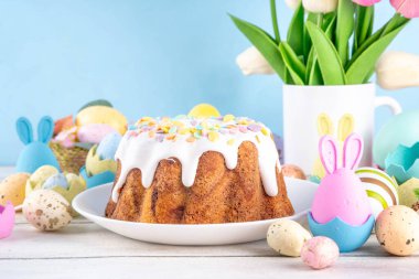 Traditional Easter cake decorated with sugar icing and sprinkles, with festive spirit decor and flower bouquet. Easter celebrations holiday table with pastel colored Easter eggs and bunny rabbits clipart